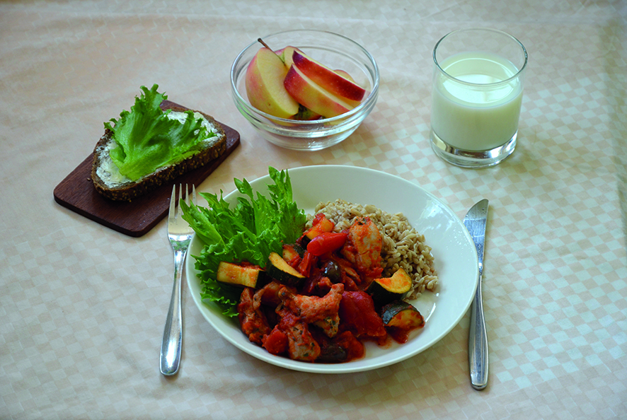 Kuvassa ateria, jossa on punainen kanapata, ruokakaura, sekaleipää, päällä levitettä ja salaatinlehtiä, maito/piimä, omena tai päärynä